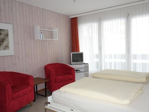 Ein Hotelzimmer mit einem Bett, zwei roten Sesseln, einem Fernseher und einem Bücherregal.