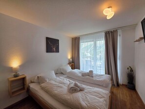 Ein Hotelzimmer mit einem Doppelbett, einem Nachttisch mit Lampe, einem Fenster mit Vorhängen und einem Wandbild.