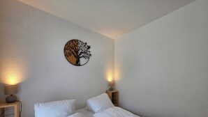 A bedroom with two single beds, a nightstand with a lamp, and a wall-mounted tree decoration. - Nicoletta 2. OG Appartement/Fewo 8-Bettwohnung Nr. 1 by Interhome (Saas-Fee)