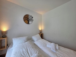 Ein Schlafzimmer mit zwei Einzelbetten, einem Nachttisch mit Lampe und einer Wanddekoration mit Baumdesign.