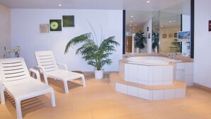 A modern bathroom with a large bathtub, two white lounge chairs, a potted plant, and a mirror reflecting the room. - Nicoletta 2. OG Appartement/Fewo 8-Bettwohnung Nr. 1 by Interhome (Saas-Fee)