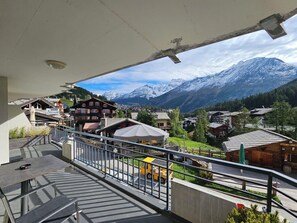 Un balcon offrant une vue sur un village de montagne, avec ses bâtiments et ses sommets enneigés.