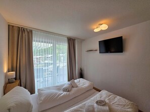 Une chambre d’hôtel avec un lit, un téléviseur fixé au mur et une fenêtre avec des rideaux.