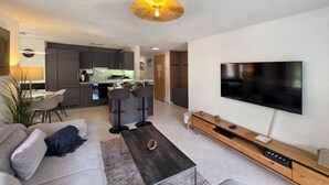 A modern living room with a flat-screen TV, a sofa, a coffee table, and a kitchen in the background. - Nicoletta 2. OG Appartement/Fewo 8-Bettwohnung Nr. 1 by Interhome (Saas-Fee)