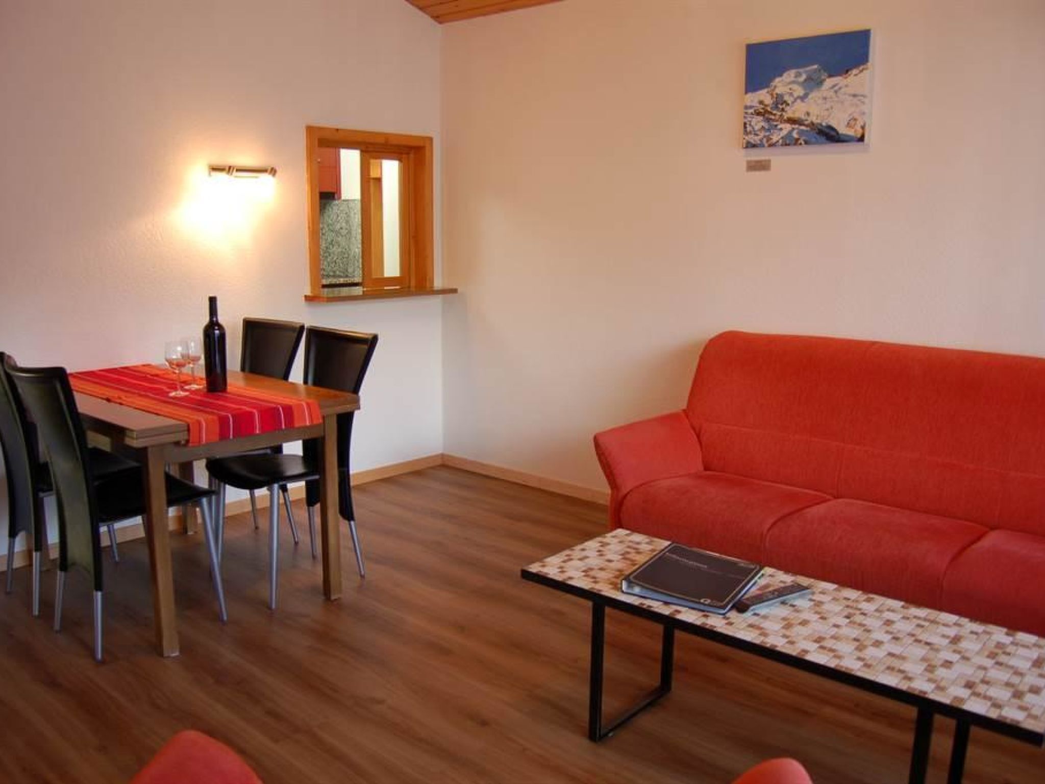 En matplats med ett bord dukat för två personer, en röd soffa och ett litet bord med en bok på.