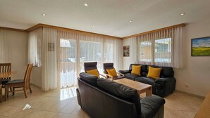 Ein Wohnzimmer mit einer Sofagarnitur, einem Holztisch und einem Essbereich mit Stühlen.