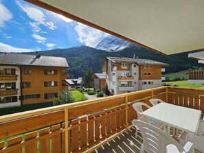 A balcony with wooden railings, a table, and chairs, overlooking a mountain and buildings. - Dominic B1 03 Appartement/Fewo 6-Bettwohnung by Interhome (Saas-Fee)