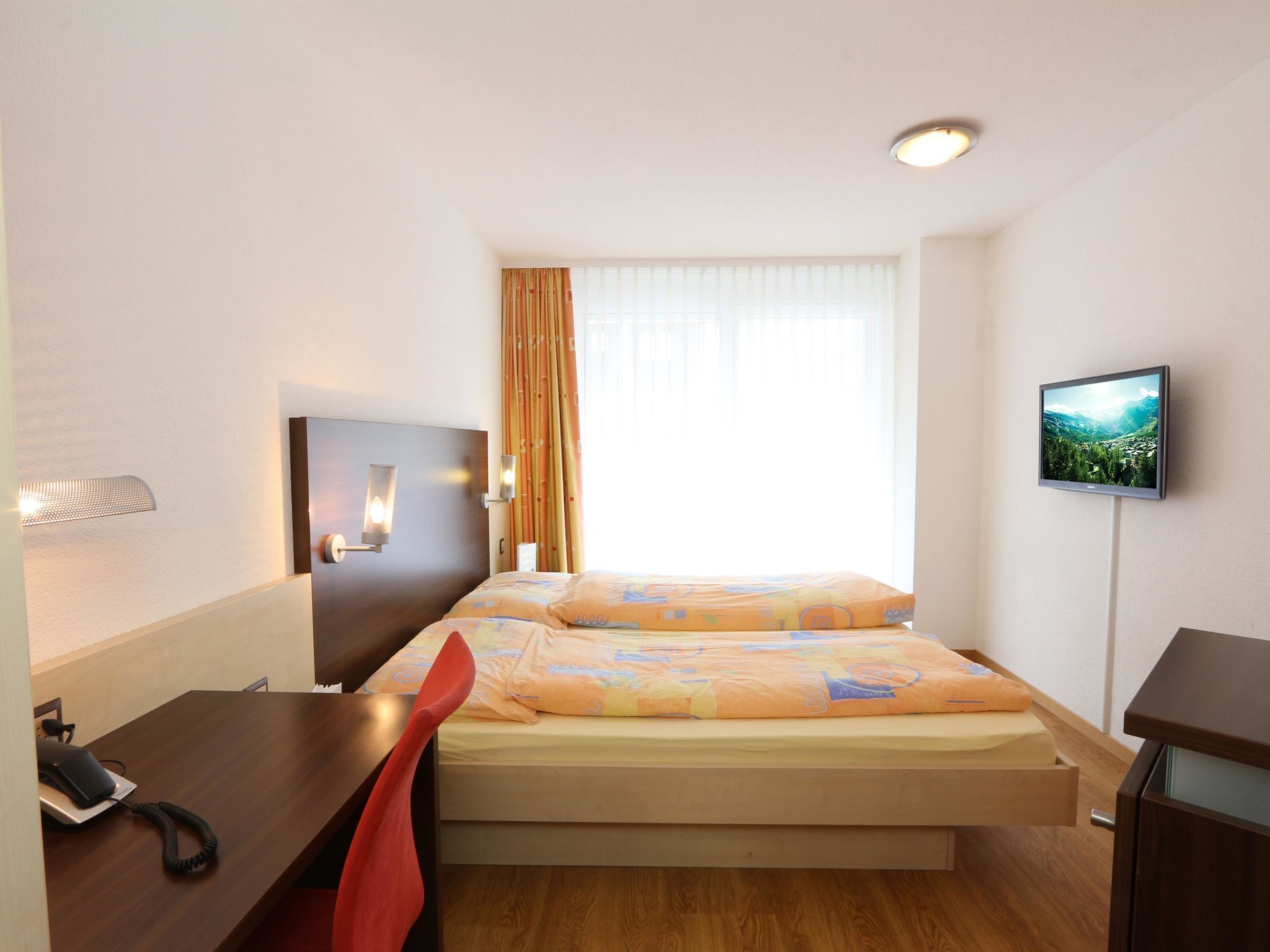 A hotel room with a bed, a desk, a chair, a TV, and a window with curtains.