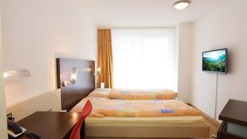 A hotel room with a bed, a desk, a chair, a TV, and a window with curtains.