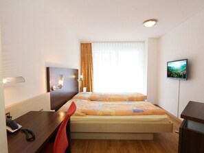 Ein Hotelzimmer mit Bett, Schreibtisch, Sessel, Fernseher und einem Fenster mit Vorhängen.