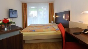 Habitación de hotel con cama, escritorio, silla, televisión y ventana con cortinas.