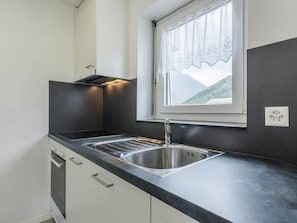 A compact kitchen with a stainless steel sink, a built-in oven, and a window with a view of a mountain landscape. - Alouette Appartement/Fewo 6-Bettwohnung Nr. 13 by Interhome (Saas-Fee)