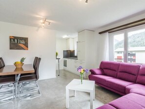 Ein modernes Wohnzimmer mit einem violetten Sofa, einem Essbereich mit Tisch und Stühlen sowie einer Küche im Hintergrund.