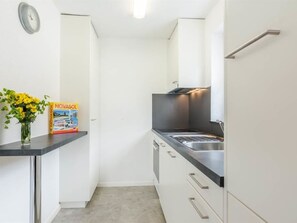 Cocina compacta con lavamanos, armarios y un reloj en la pared.