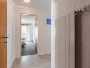 A hallway with a wooden door on the left, a radiator on the right, and a glimpse of a bedroom with a bed and window in the background. - Alouette Appartement/Fewo 6-Bettwohnung Nr. 13 by Interhome (Saas-Fee)