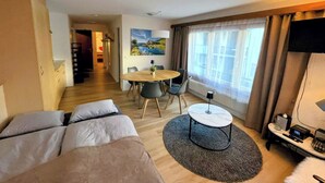 A hotel room with a bed, a dining table with chairs, a round coffee table, a TV, and a large window with curtains. - Cabane 3 Appartement/Fewo Holiday-Schöner Wohnen by Interhome (Saas-Fee)
