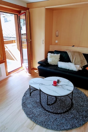 Ein Wohnzimmer mit einer schwarzen Couch, einem runden Couchtisch und einem großen Fenster.