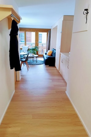 Ein Flur, der in einen Essbereich mit Tisch, Stühlen, einer Couch und einer Pflanze führt.
