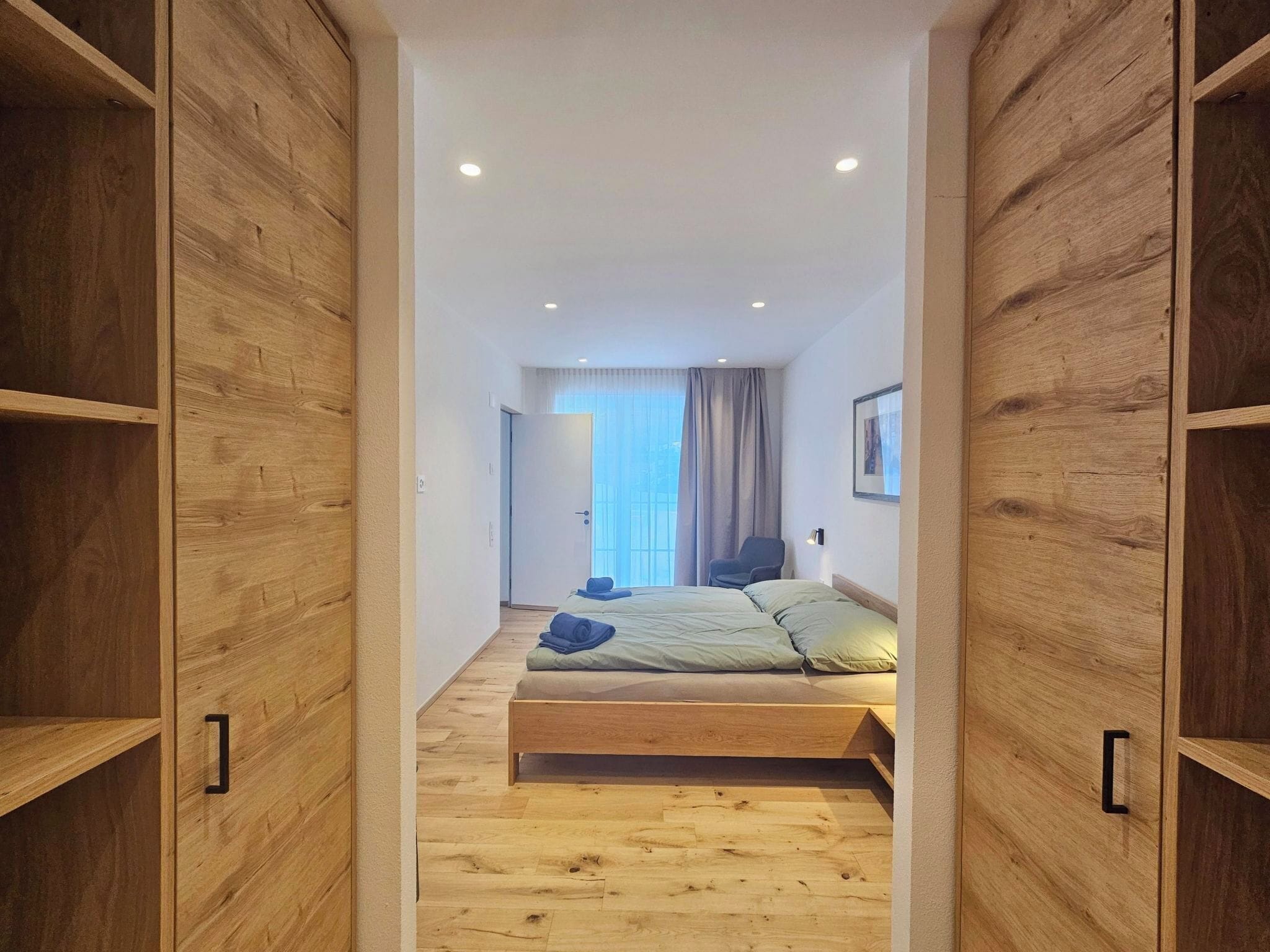 Une chambre avec un lit en bois, une chaise et une vue sur l’extérieur.