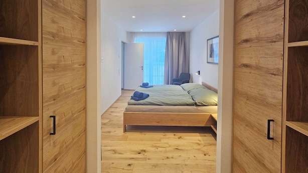 A bedroom with a wooden bed, a chair, and a view of the outside. - Silberdistel EG Appartement/Fewo Appartement/Fewo by Interhome (Saas-Fee)
