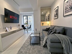 A modern living room with a grey sofa, a coffee table, a TV mounted on the wall, and a dining area with chairs and a table. - Bucharest Central by Skyline Stays (Bucharest)