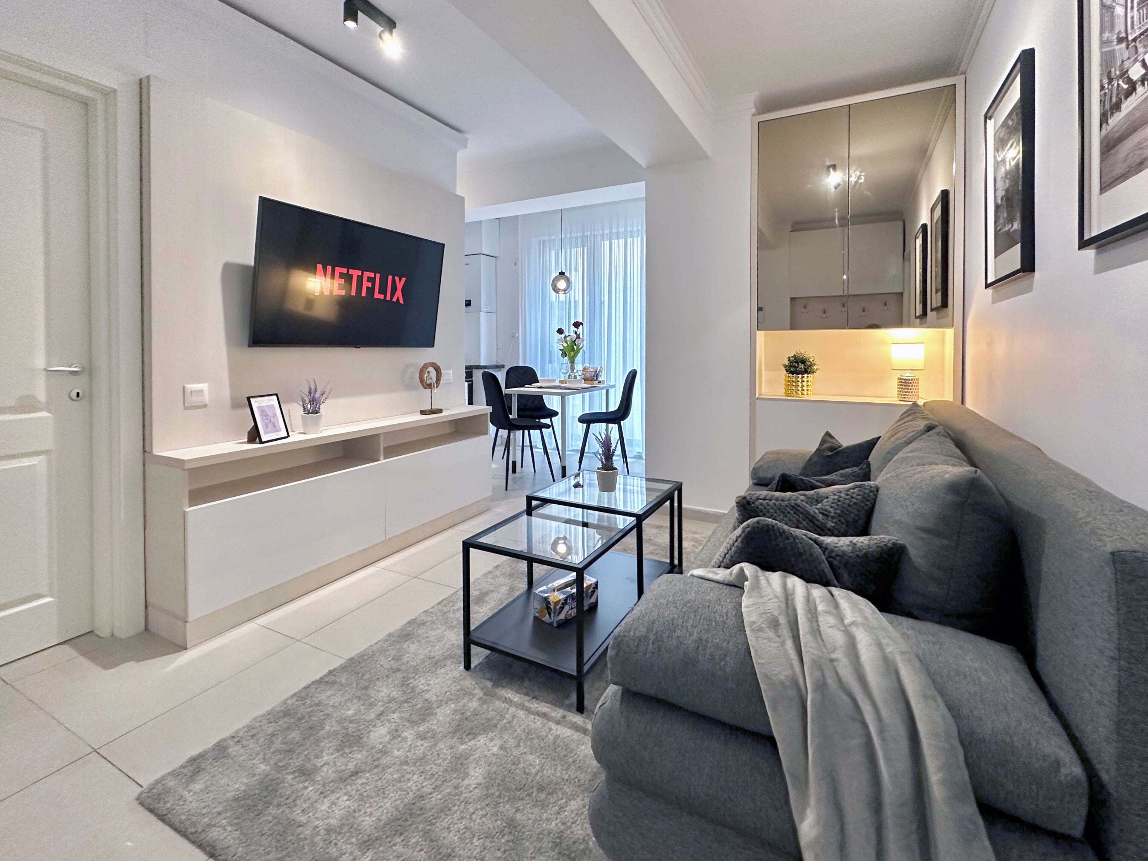 Een moderne woonkamer met een flatscreen televisie, een bank, een salontafel en een eethoek met stoelen en een tafel.