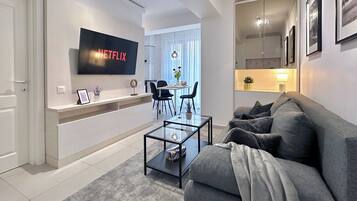 Een moderne woonkamer met een flatscreen televisie, een bank, een salontafel en een eethoek met stoelen en een tafel.