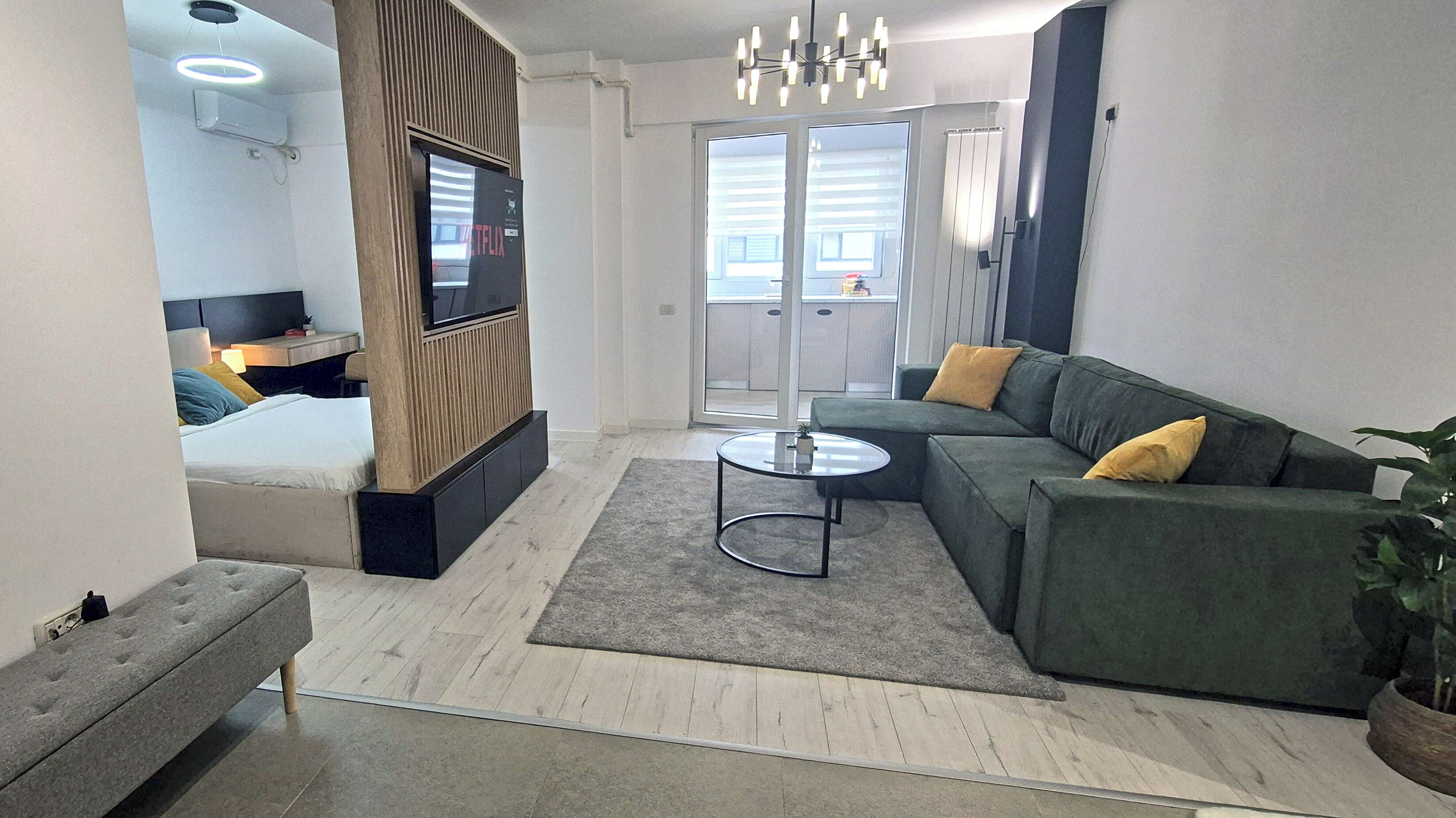 A modern living room with a green sofa, a small round coffee table, and a TV mounted on a wooden panel.