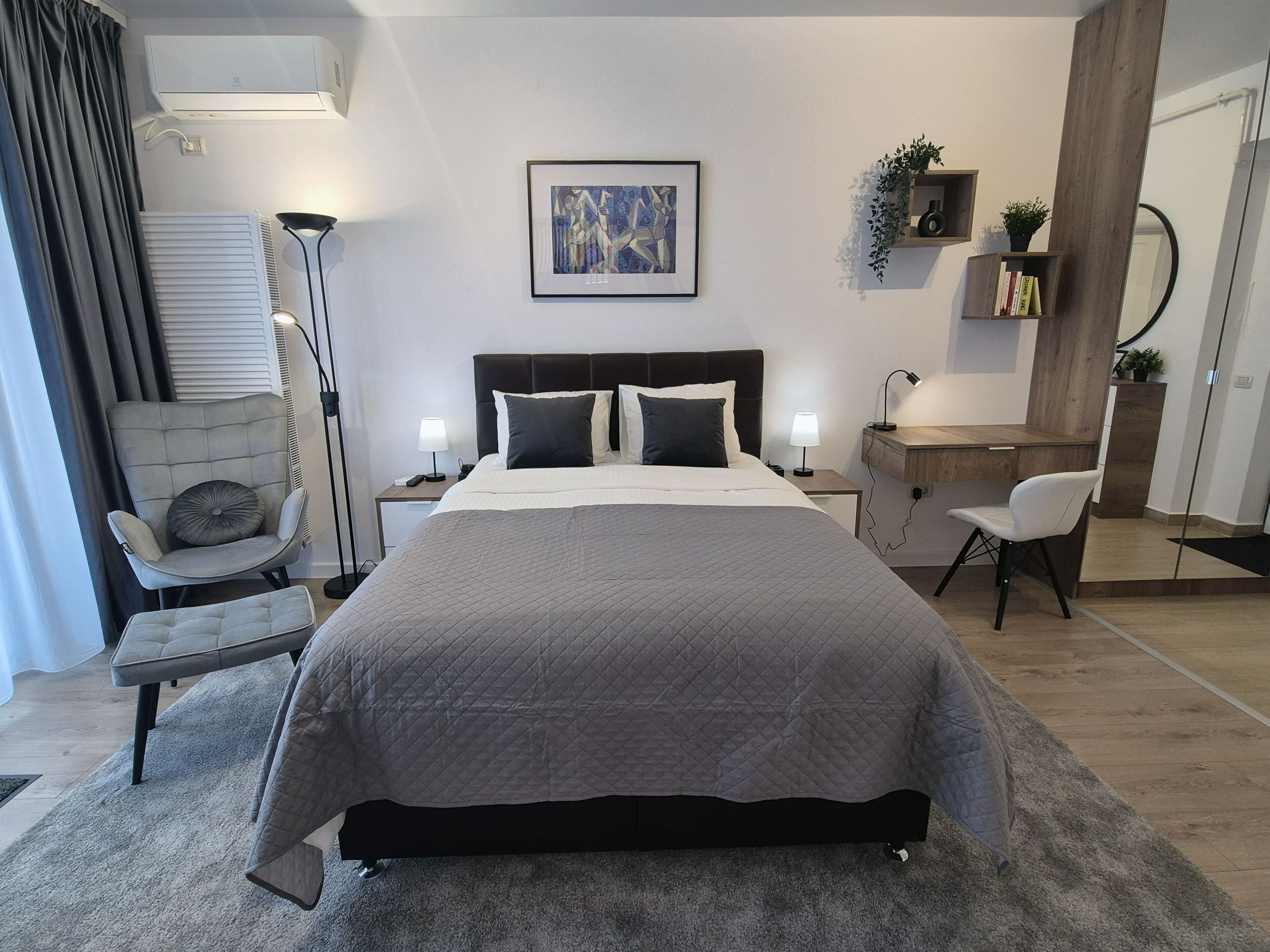 Un dormitorio moderno con una cama grande, mesitas de noche, una silla, un escritorio y una estantería de pared.