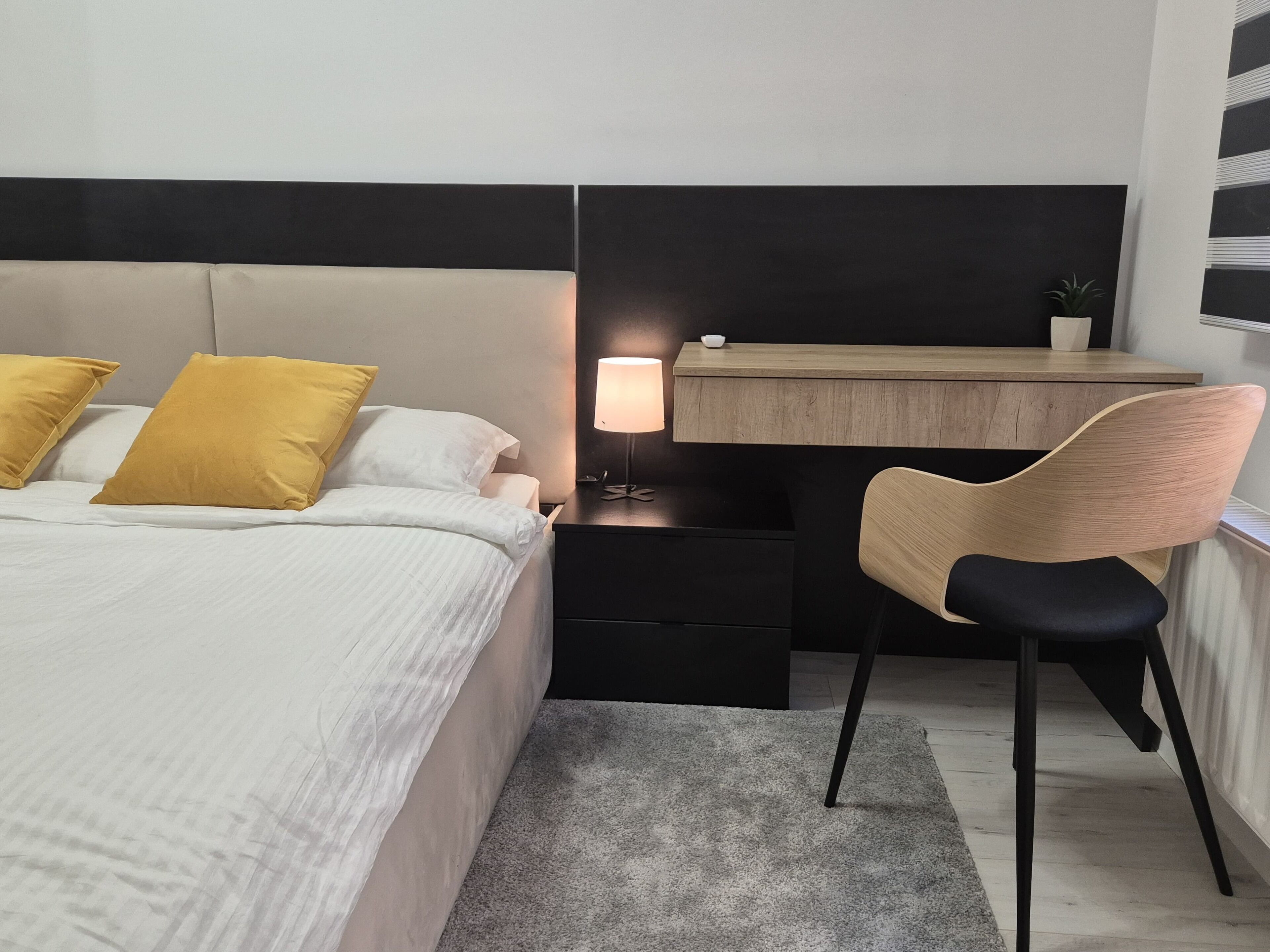 Un dormitorio moderno con cama, mesita de noche, escritorio, silla y lámpara.