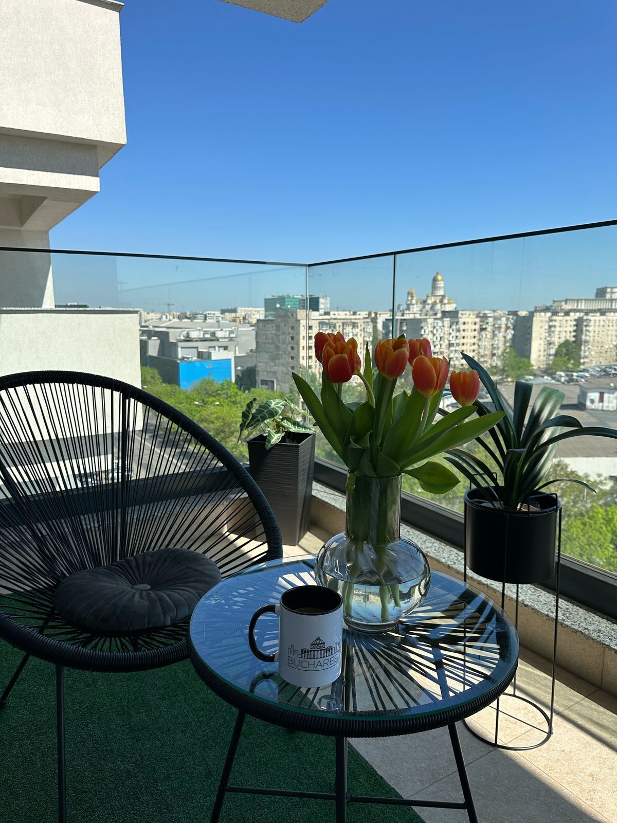 A balcony with a glass table, a chair, a vase with tulips, and a mug.
