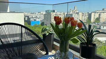 A balcony with a glass table, a chair, a vase with tulips, and a mug.