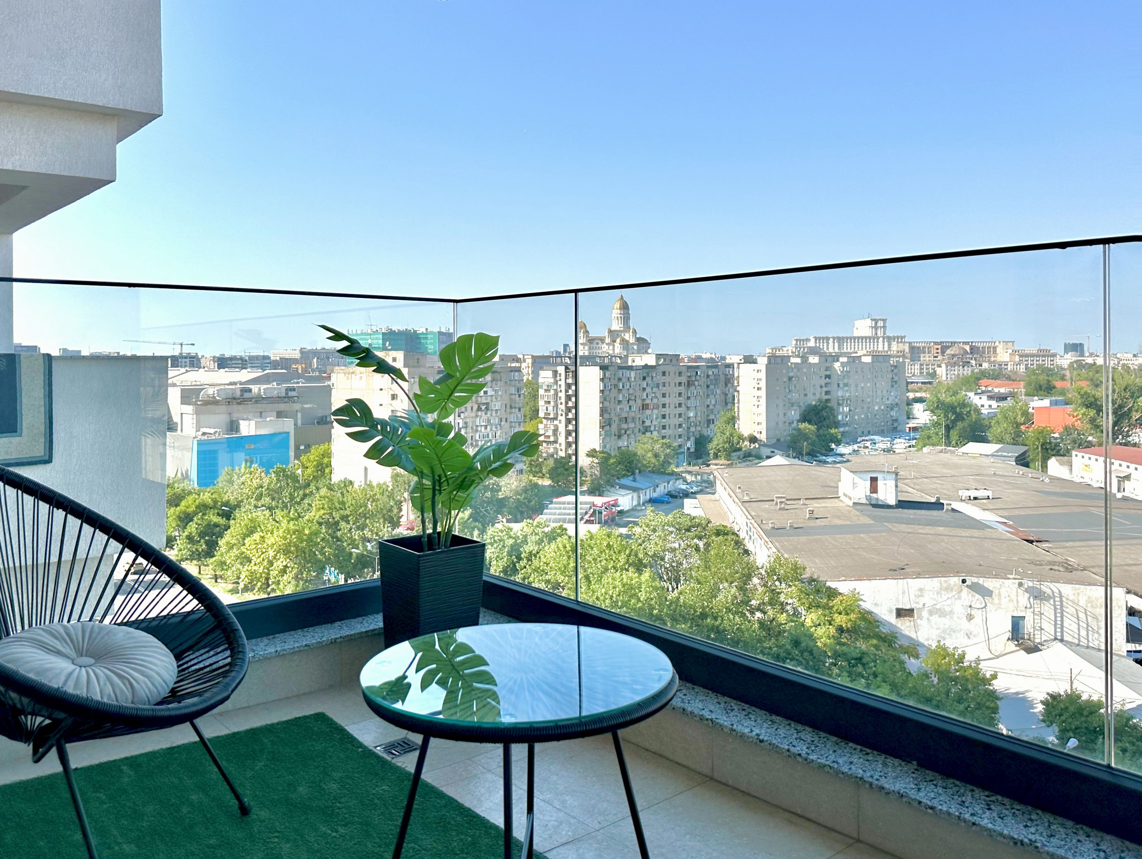 A balcony with a view of a cityscape, a potted plant, a chair, and a small table.
