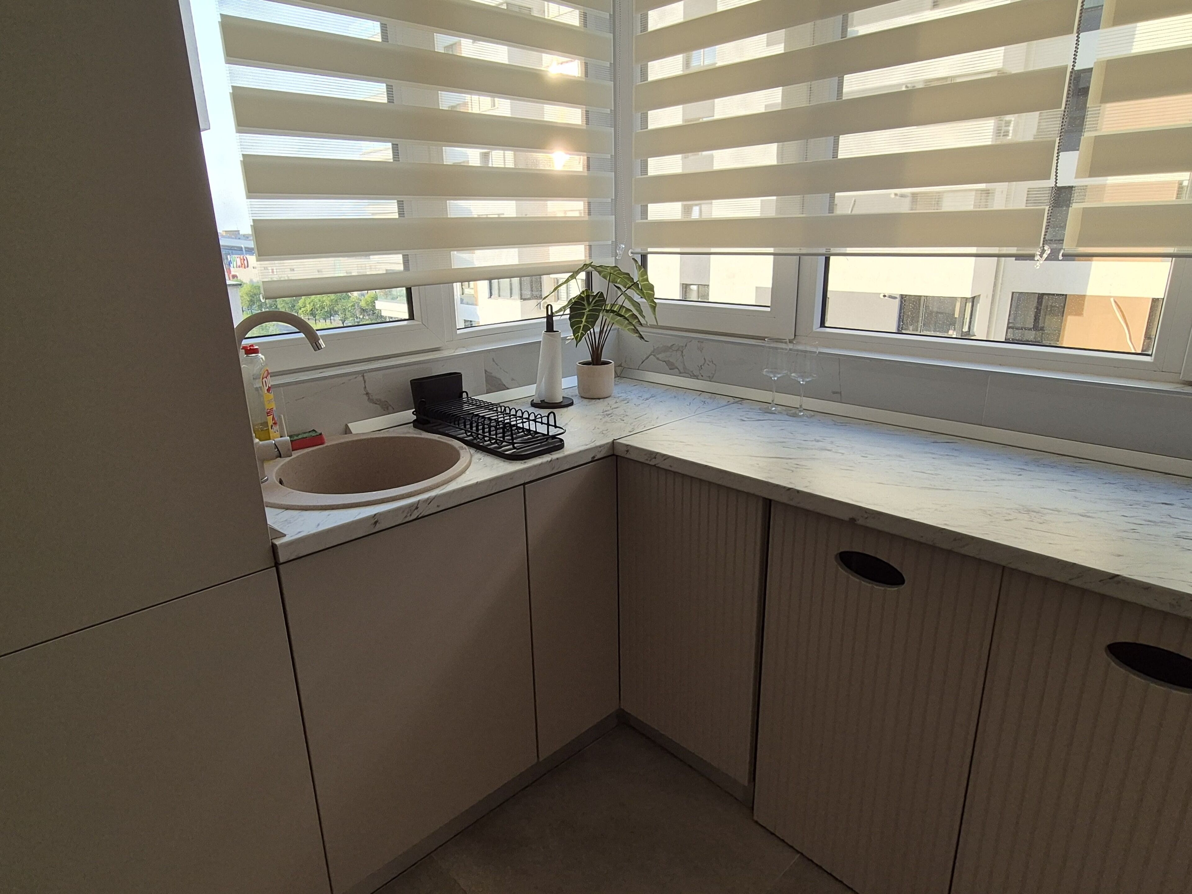 A modern kitchen with a sink, countertop, and window blinds.