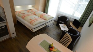 Ein kleines Hotelzimmer mit Bett, einem Esstisch mit Früchten, einem Stuhl und einem Fernseher.