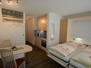 A compact room with a kitchenette, a dining area with a table and chairs, and a bed with a floral bedspread. - Kandahar Appartement/Fewo 2-Bettwohnung Nr. 1 by Interhome (Saas-Fee)
