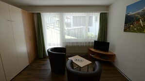 Ein Zimmer mit Fernseher, zwei Sessel, einem kleinen Tisch und einem Bild an der Wand.