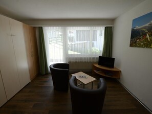 Una habitación con televisión, dos sillones, una mesita y un cuadro en la pared.