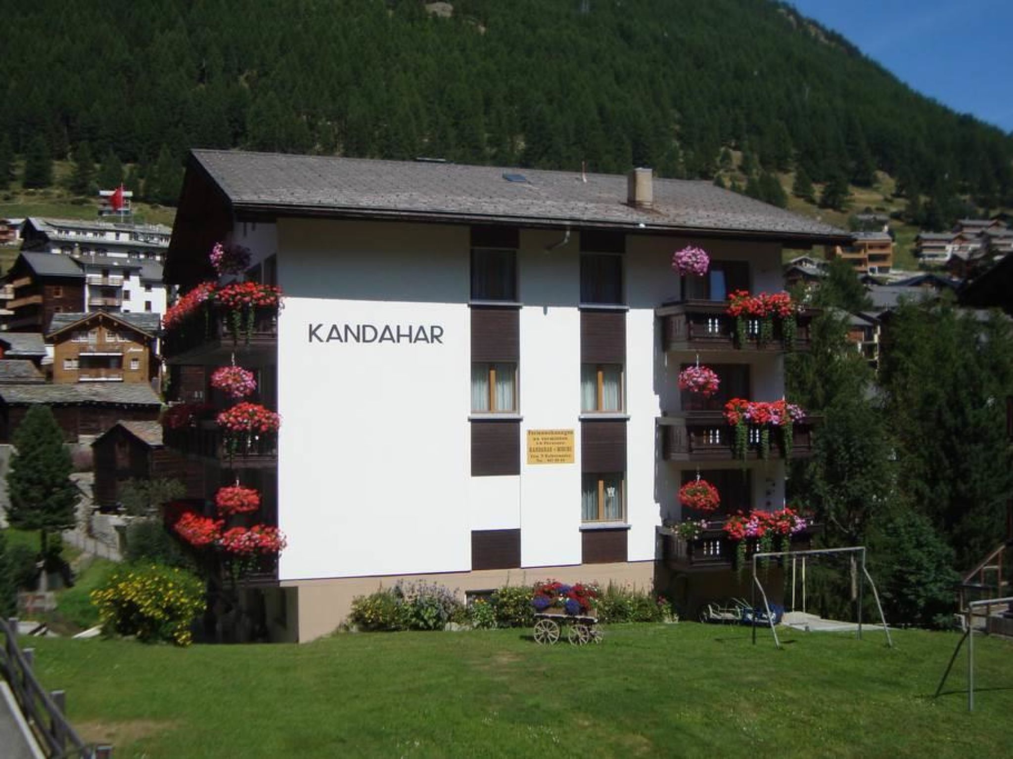 A building with the name 'KANDAHAR' on its facade, surrounded by greenery and a mountainous backdrop.