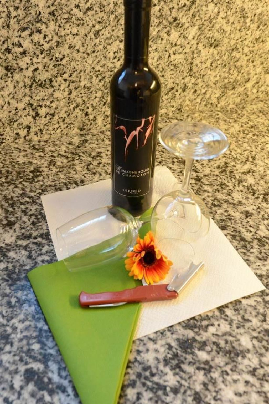 Une bouteille de vin, un verre à vin, un couteau et une fleur sur un comptoir.