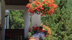 Ein Haus mit Veranda, einem Topf mit roten Blumen und einem kleinen Holzschemel.