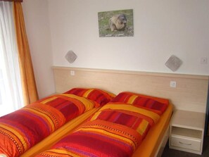 Un lit double avec une parure de lit à rayures, une table de chevet avec un tiroir et un tableau représentant une marmotte accroché au mur.