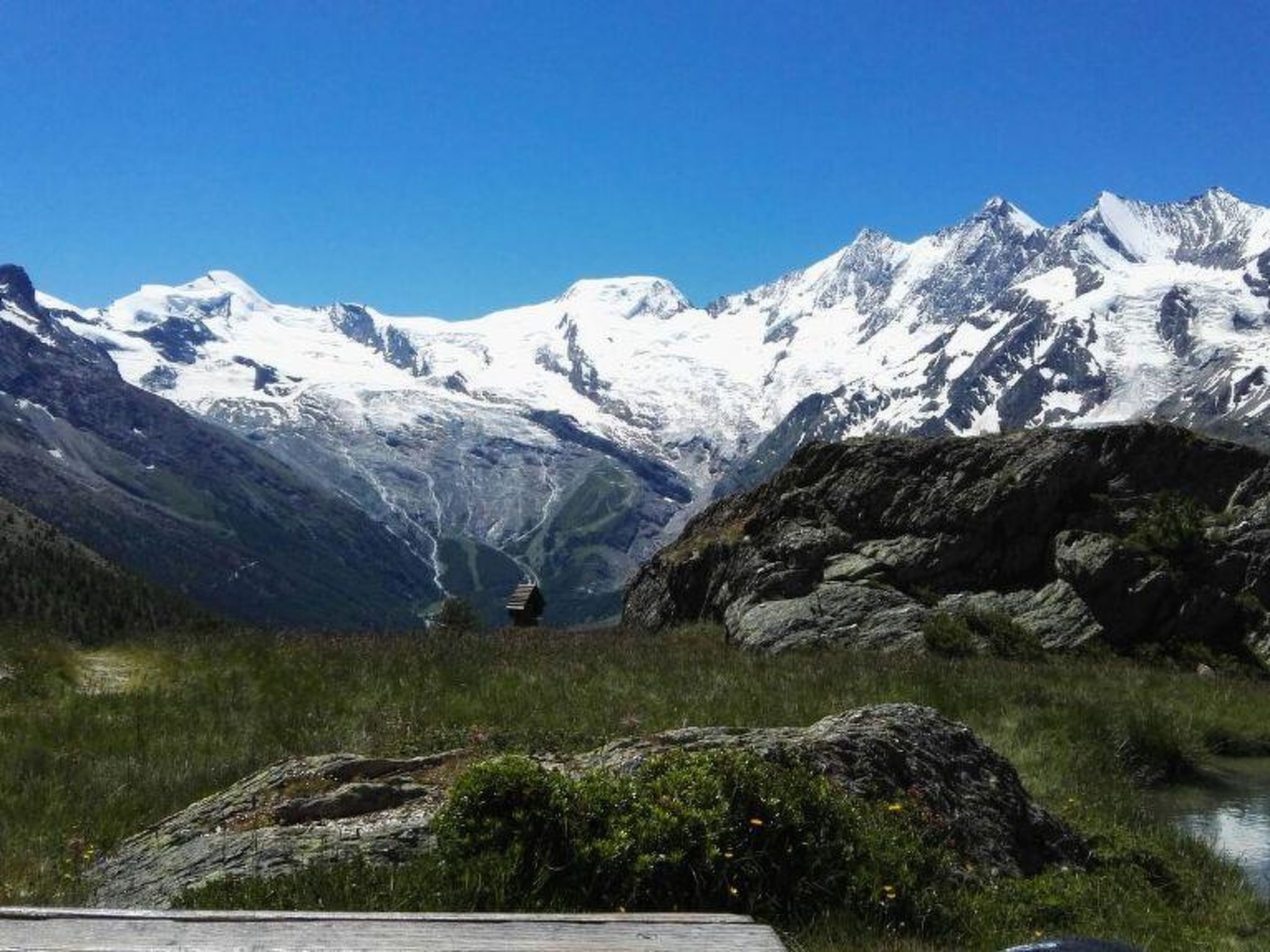 A mountainous landscape with snow-capped peaks, a small cabin, and a rocky foreground.