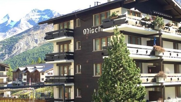 A multi-story building with balconies, a sign reading 'Misch,' and a mountainous backdrop. - Mischi Appartement/Fewo 2-Bettwohnung Nr. 15 by Interhome (Saas-Fee)