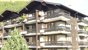 A multi-story hotel with balconies, a mountain backdrop, and a large evergreen tree in the foreground. - Mischi Appartement/Fewo 2-Bettwohnung Nr. 15 by Interhome (Saas-Fee)