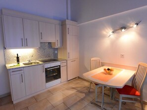 Een kleine keuken met een eethoek, inclusief kastjes, een spoelbak, een oven en een tafel met stoelen.