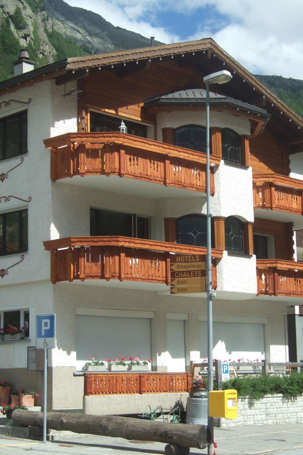 Ein mehrgeschossiges Gebäude mit Balkonen, einem Schild für Hotels und Chalets und einem Parkplatzzeichen.