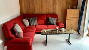 En röd, modulbaserad soffa med mönstrade kuddar, ett soffbord i marmor och ett träskåp.