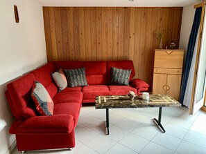A red sectional sofa with patterned cushions, a marble coffee table, and a wooden cabinet. - Bergröschen Appartement/Fewo 5-Bettwohnung by Interhome (Saas-Grund)