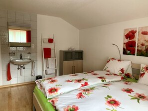 Une chambre à coucher comprenant un lit, une table de chevet, une commode, un miroir et une salle de bain avec un lavabo et un porte-serviettes.